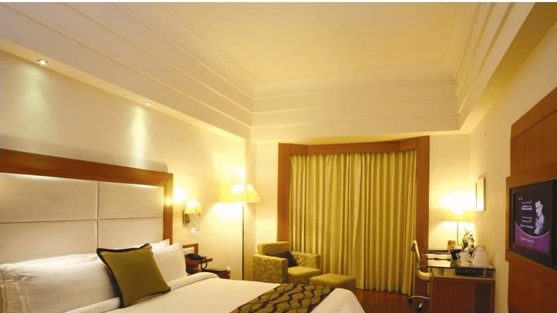A Deluxe King Size Bed room at Ambrosia Sarovar Portico, Haridwar, featuring a king size bed, a flat-screen television, a working desk and a seating area. 