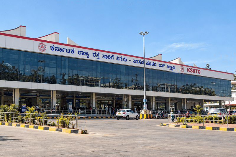 Long glass-fronted Hassan KSRTC Bus Stand building with its Kannada name board and KSRTC sign