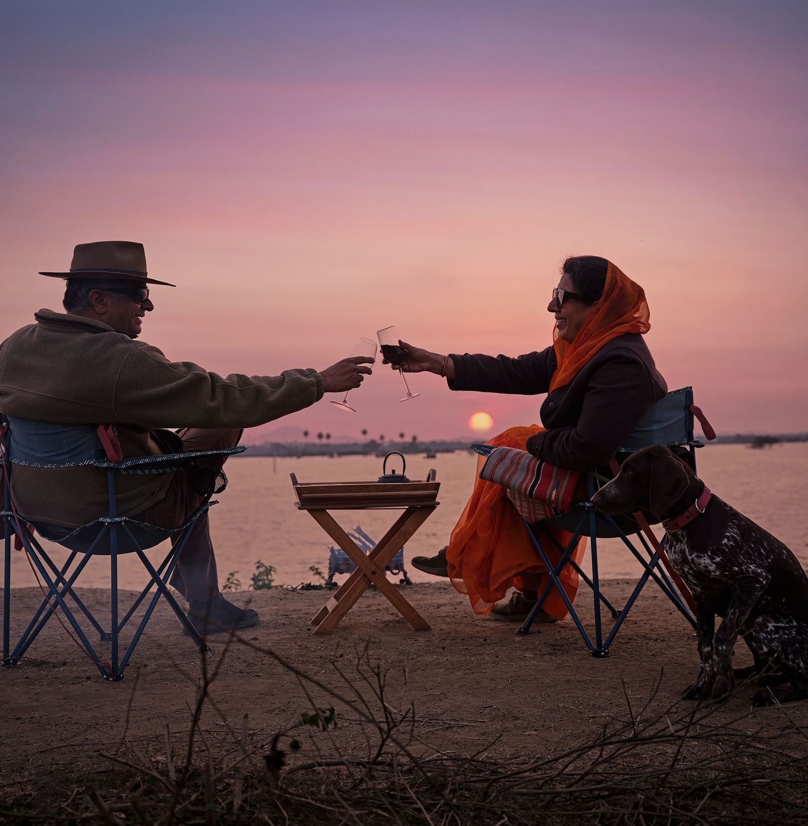 image of a couple enjoying the sunset as they cling wine glasses at Dev Shree, Deogarh