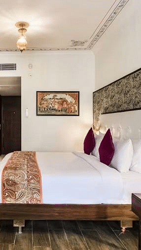 A well-lit hotel room with a plush bed, pillows, a desk, and a TV.- Bamboo Saa Resort & Spa, Udaipur