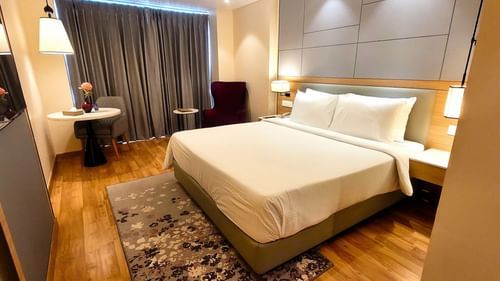 A wide-angle shot of the Executive Room at Golden Sarovar Portico, Amritsar, showcasing the spacious layout with the plush king bed, a bedside table, and the elegant, modern drcor.