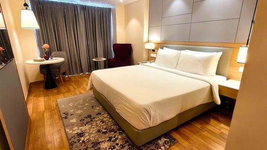 A wide-angle shot of the Executive Room at Golden Sarovar Portico, Amritsar, showcasing the spacious layout with the plush king bed, a bedside table, and the elegant, modern drcor.