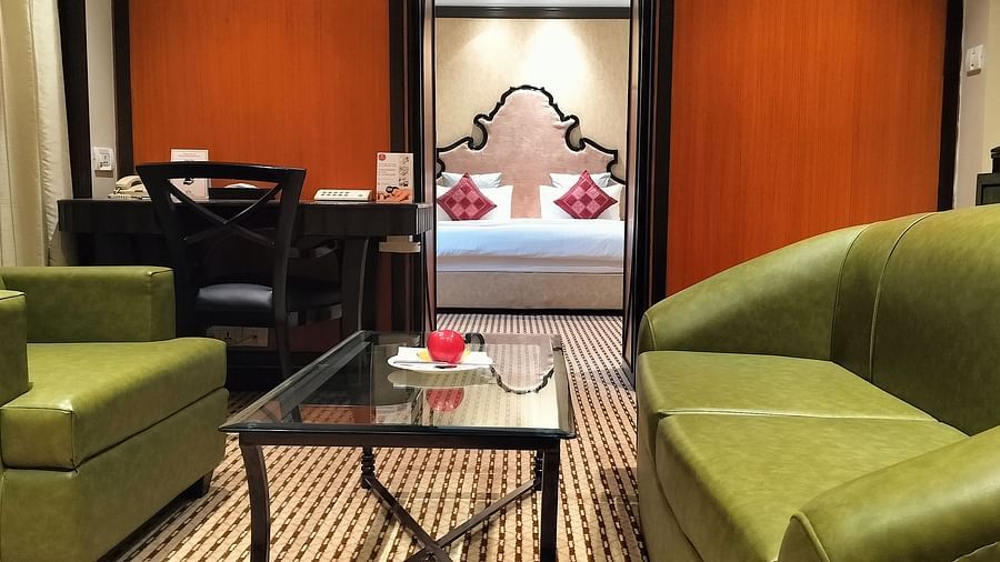 Hotel room with twin chairs, a coffee table, and a bed framed by lamps and wall art.