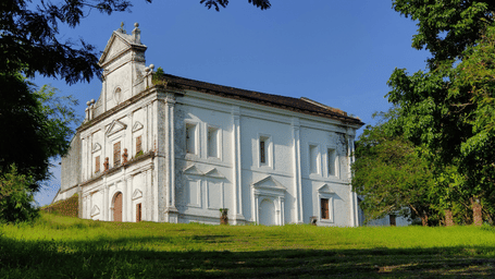 Facade of the Chapel of Our Lady of the Mount with rectangular windows and sloping roof, standing on a grassy lawn with trees around