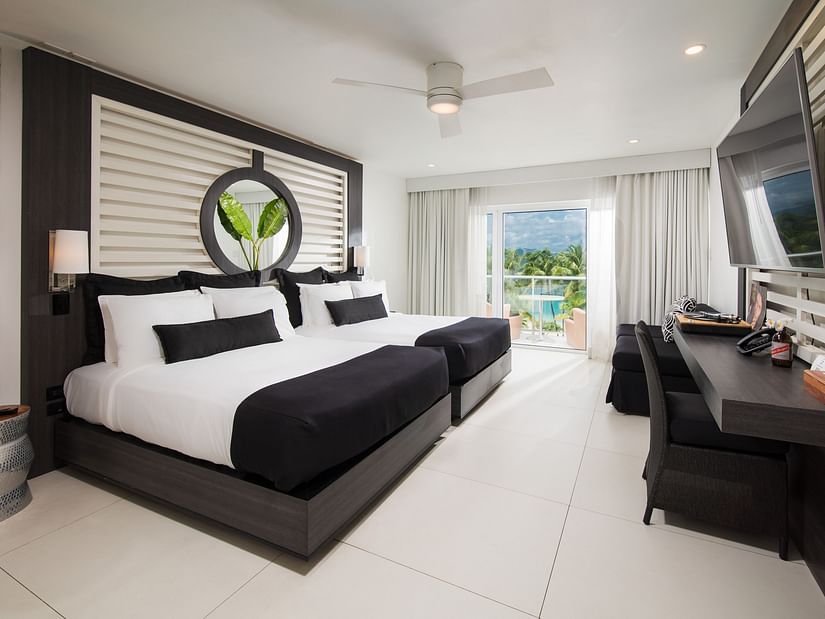 A image of a hotel room with twin beds, a balcony offering sea views, and a wall-mounted television - S Hotel Montego Bay, Jamaica