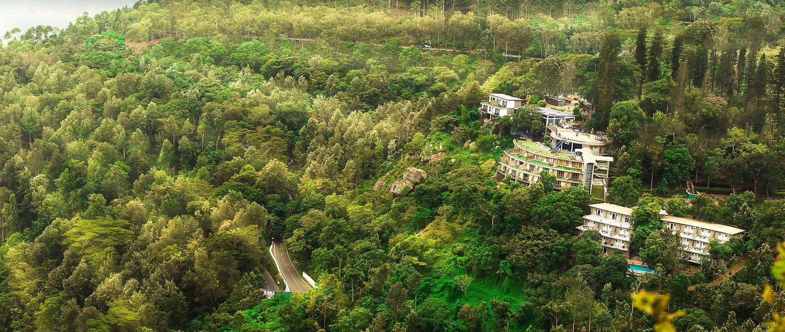 Drone shot of the hotel surrounded by mountains with sun light hitting the lush greenery - Great Trails Yercaud by GRT Hotels