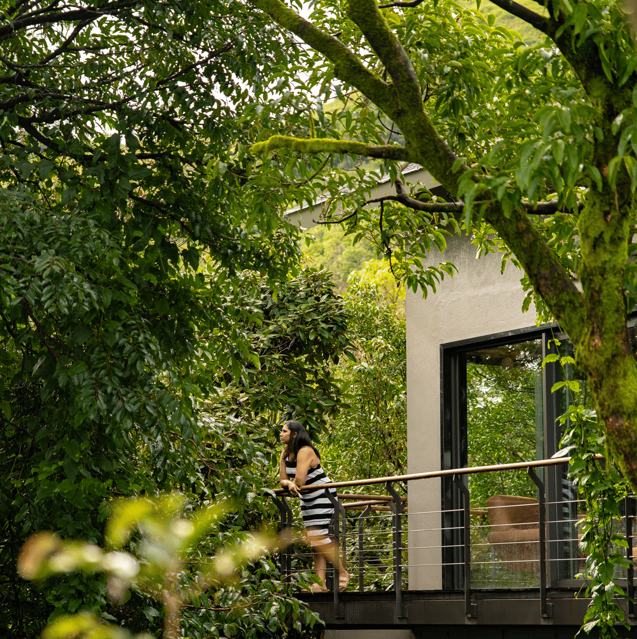 A person stands on a balcony in a modern building at Stanley Revelation, surrounded by lush green trees.