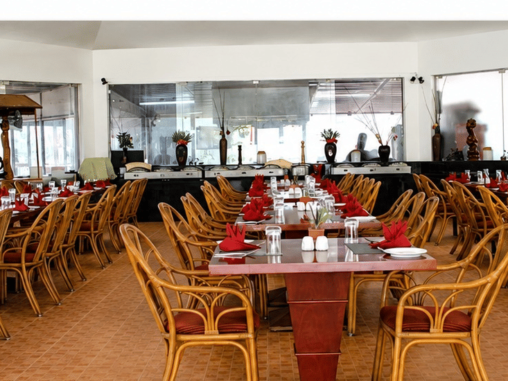 Kapi Restaurant dining area with wicker chairs and red table accents at Chariot Beach Resorts, offering a warm and inviting atmosphere