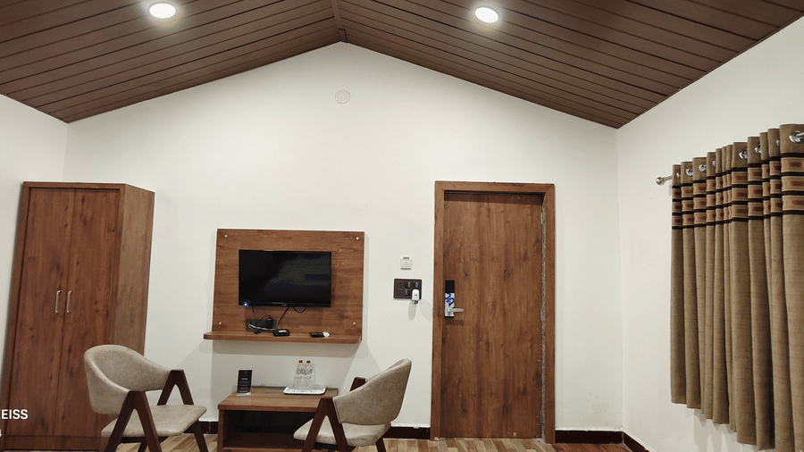 Hotel room sitting area with two chairs, wooden TV unit, wardrobe, striped curtains, vaulted wood ceiling, and a smart door lock.
