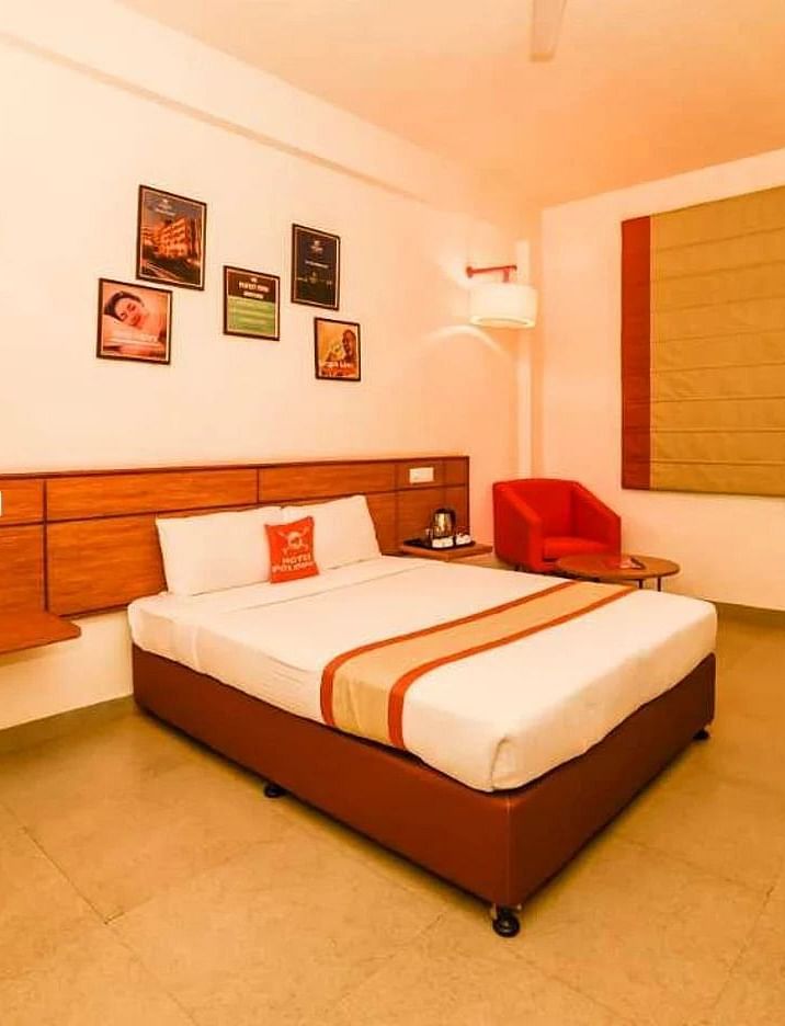 a spacious room with a queen size bed placed in the middle with small photo frames hung on the wall - Max Hotel Jabalpur