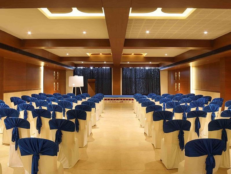 House Boat Hall at Uday Backwater Resort featuring chairs arranged in a way that they are facing the podium in front of them with a blue colour backdrop under warm lighting