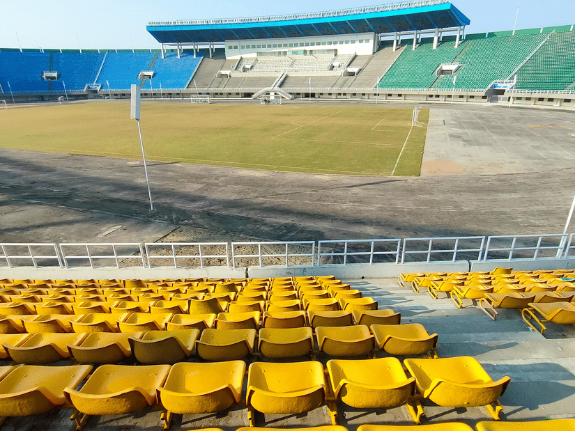 A view from the stands of a football stadium with other stands, the pitch, lights, and a running track in view.