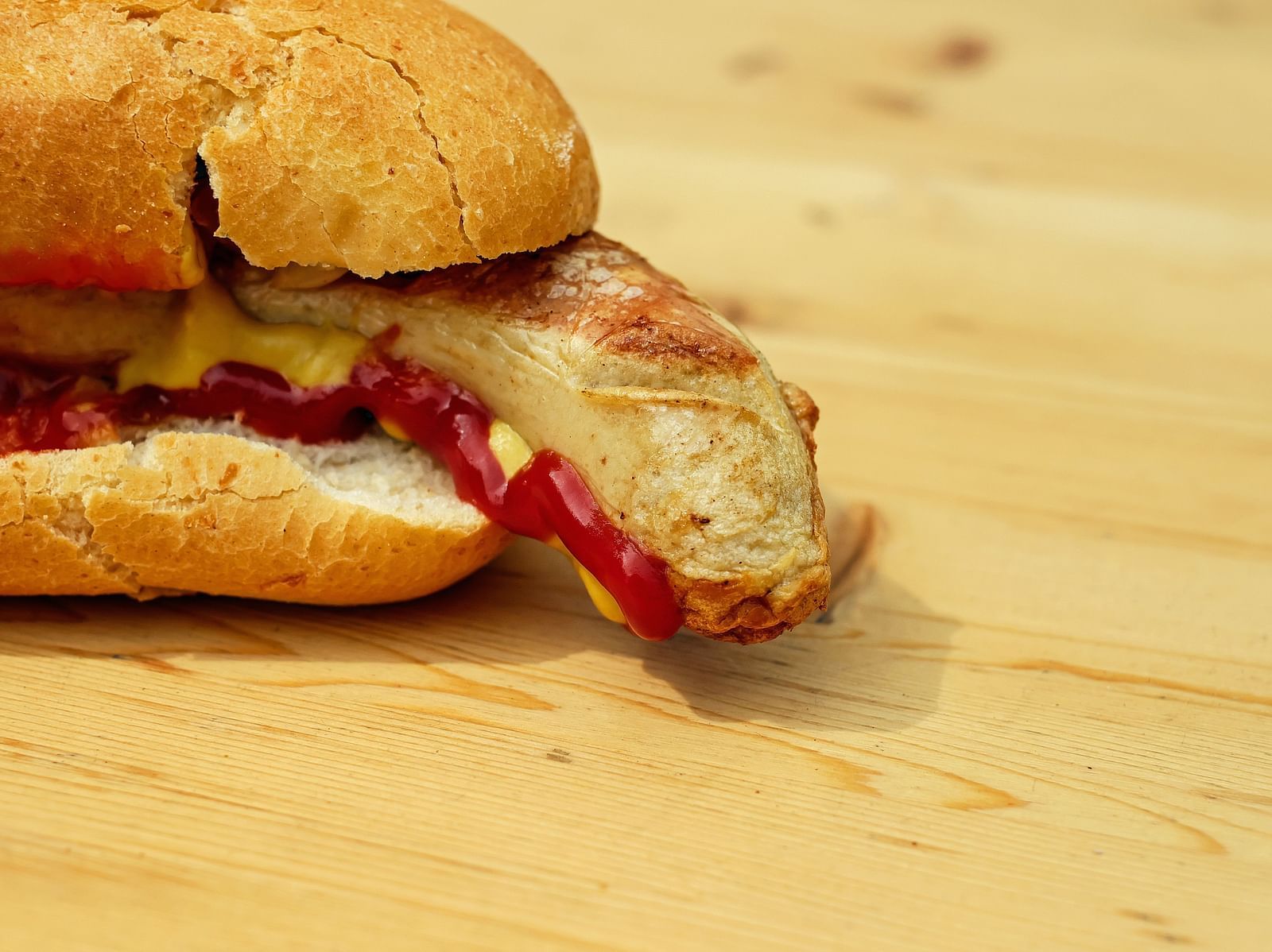 A close up shot of a bun with sausage inside it having mustard and ketchup on it.