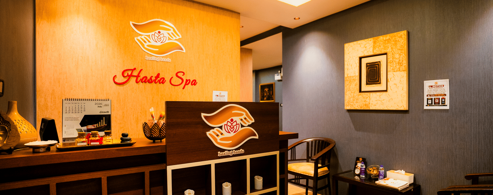 Hasta Spa reception with the healing hands logo on a timber wall, oil bottles on the counter and waiting chairs at Ilara Hotels & Spa, Tada.