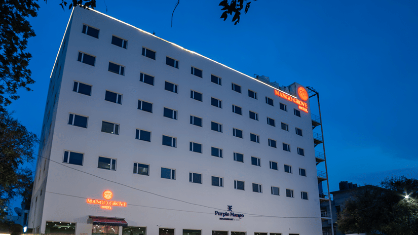 Hotel exterior lit up at night with street traffic in the foreground at Mango Grove Hotel.
