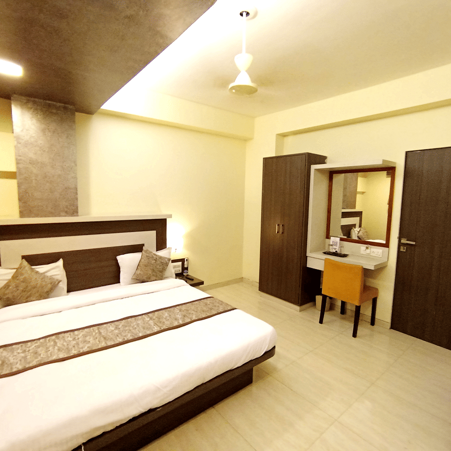 Executive room interior featuring a large bed with a decorative runner, dressing table, and dark wood wardrobe.