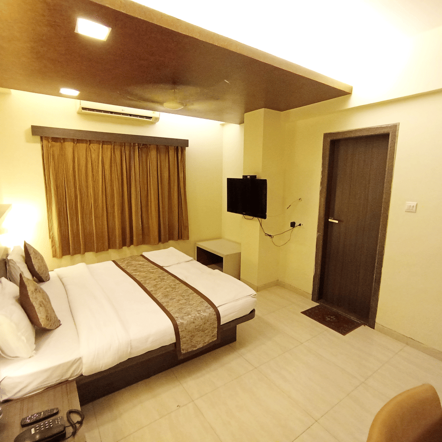 executive room  interior showcasing a double bed, wall-mounted television, and heavy gold-brown window curtains.