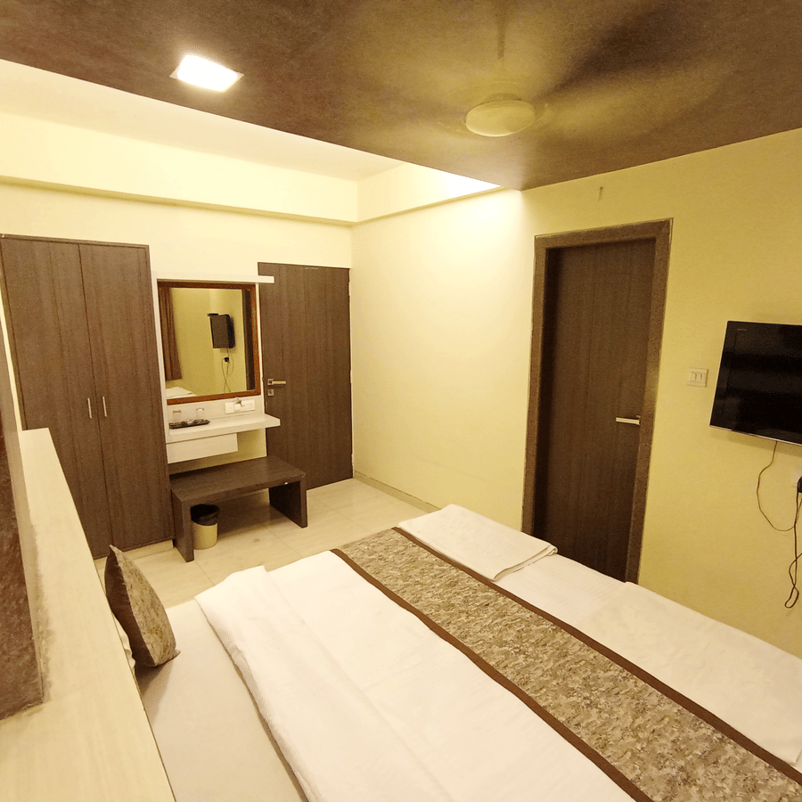 Angled view of executive room featuring a double bed, wall-mounted television, wardrobe, and vanity dresser.