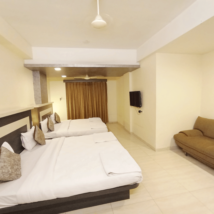 Spacious hotel room interior featuring two large beds in the background and a long brown sofa on the side.