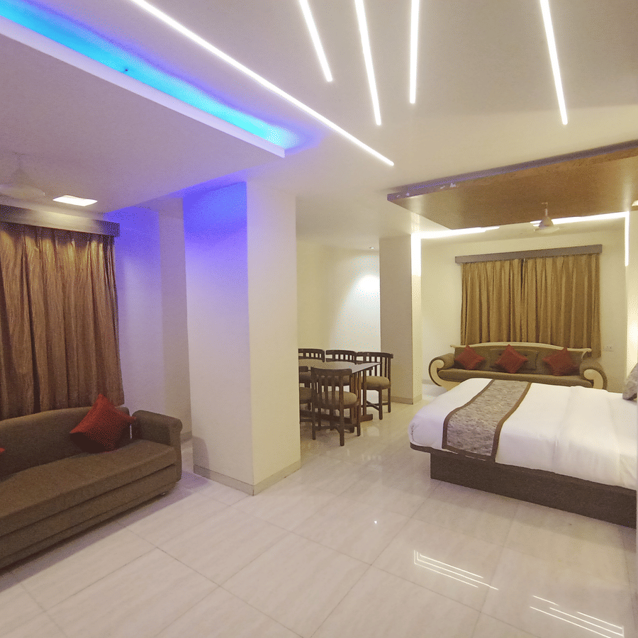 Suite room featuring bright white ceiling lights, a brown sofa with red pillows, and a bed in the background.