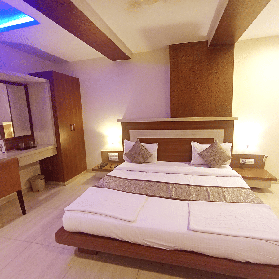 front view of a well-furnished suite room showcasing a double bed, wooden desk with a chair, and illuminated headboard.