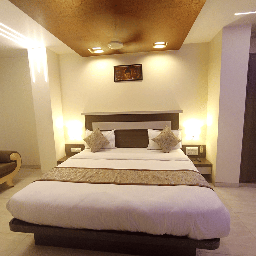 Suite room  with a double bed, warm bedside lamps, and a glimpse of a sofa seating area on the left.