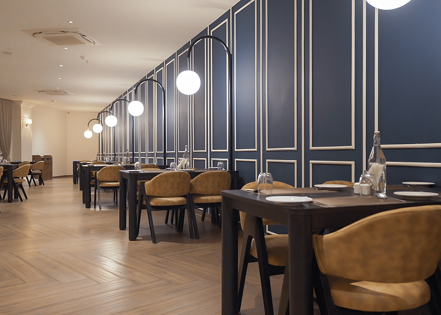 alt-text Overview shot of the restaurant at Pride Resort, Rajkot with navy blue coloured walls giving an elegant look