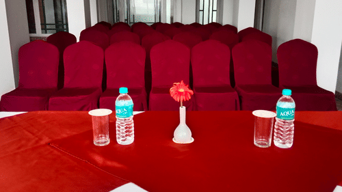 A hall setup with chairs and a table in the middle, showcasing a water bottle and a decorative flower vase