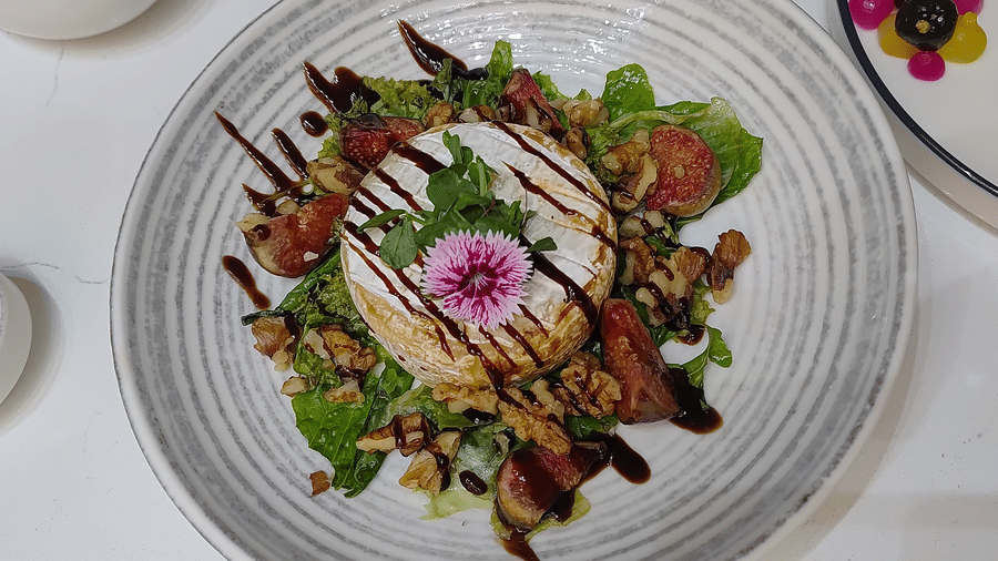 A food item garnished with leafy vegetable, herbs, other vegetables, flower, and sauce at The Wild Fork restaurant in La Marvella, Bengaluru.