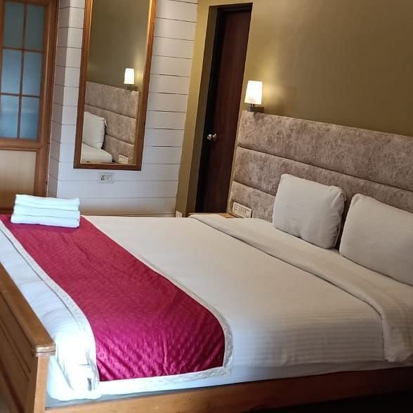 A king size bed with couple of lamps lit on both sides of the headboard and a mirror mounted on the wall next to it at Damanganga Valley Resorts