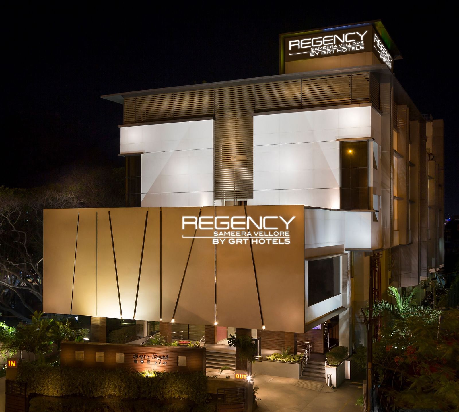  Modern multi-story hotel building with warm lighting, a prominent hotel sign, and landscaped grounds