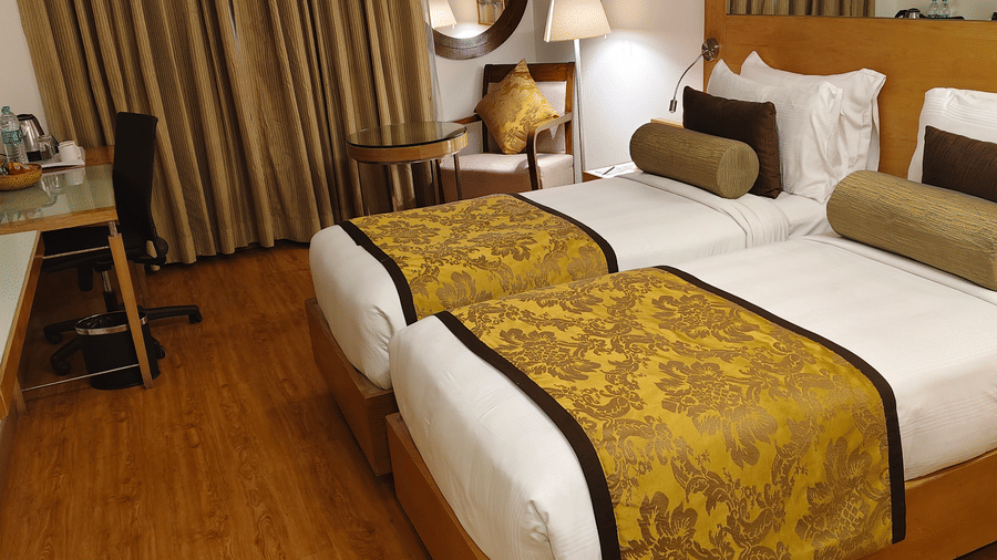 A view from the corner of the Deluxe Twin Room at Pride Premier Chennai. Two single beds sit on the right, while a work desk with a chair and television screen are on the left.