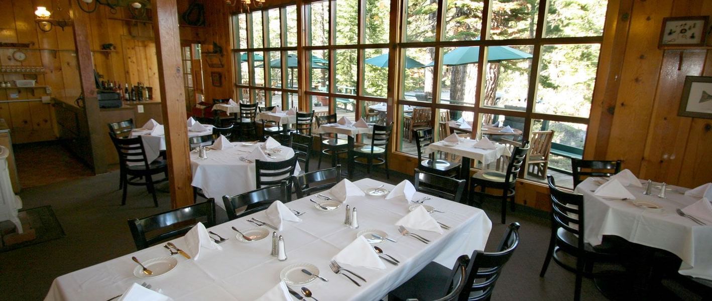 Kit Carson Lodge restaurant with set tables, wooden walls, and large windows overlooking trees.