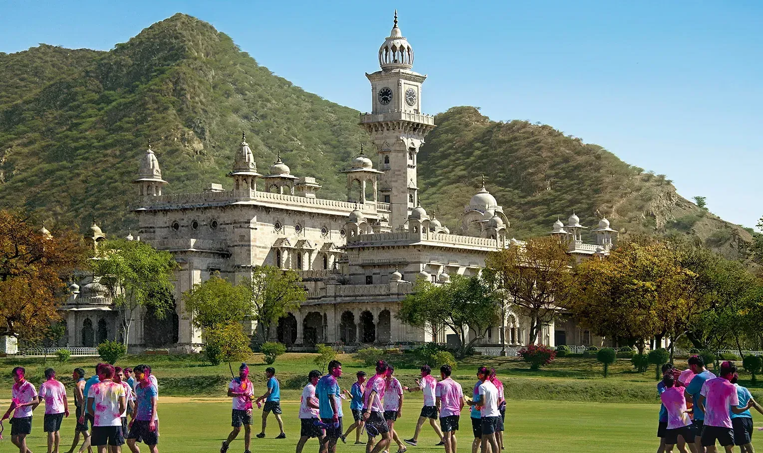 facade image of the mayo college with a huge green lawn in the foreground with adolescent kids roaming around