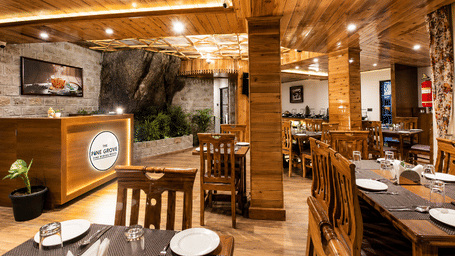 A dining area with wooden tables, chairs, a reception counter, and decorative wall art at Valmere Lungta Boutique Hotel & Spa, Darjeeling.