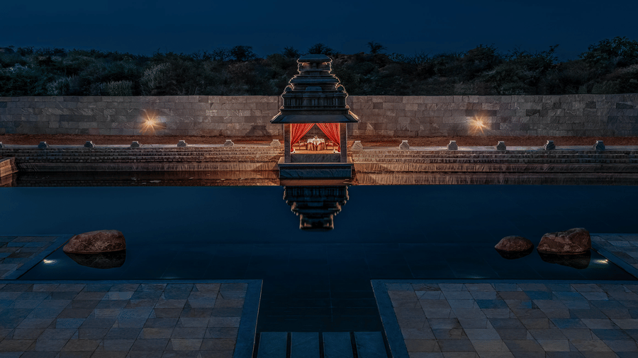 Infinity pool with temple pavilion reflection at night at Evolve Back Hampi