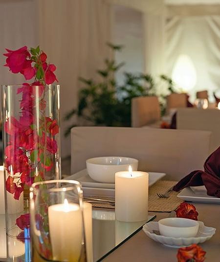 An indoor table setting with candles, flowers, and place settings - Shreyas Retreat