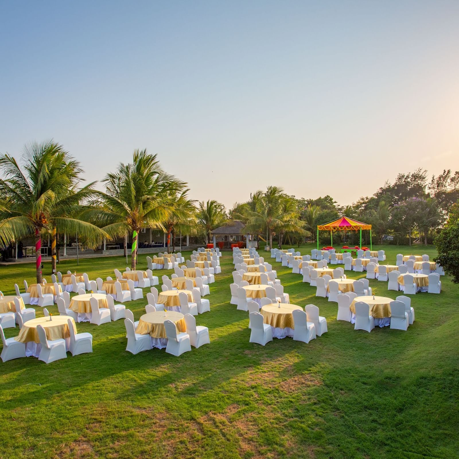 An outdoor event space on a green lawn with numerous round tables and chairs, set up for a gathering under a bright sky with palm trees | Grande Pavillion | Grand Bay Resort and Spa