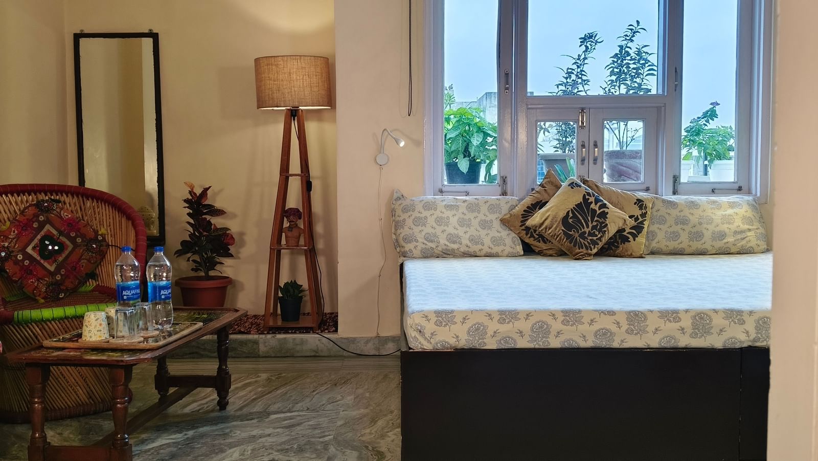 Bedroom with double bed, two chairs, small table, lamp, mirror and window at Jaypore360 Homestay in Jaipur.
