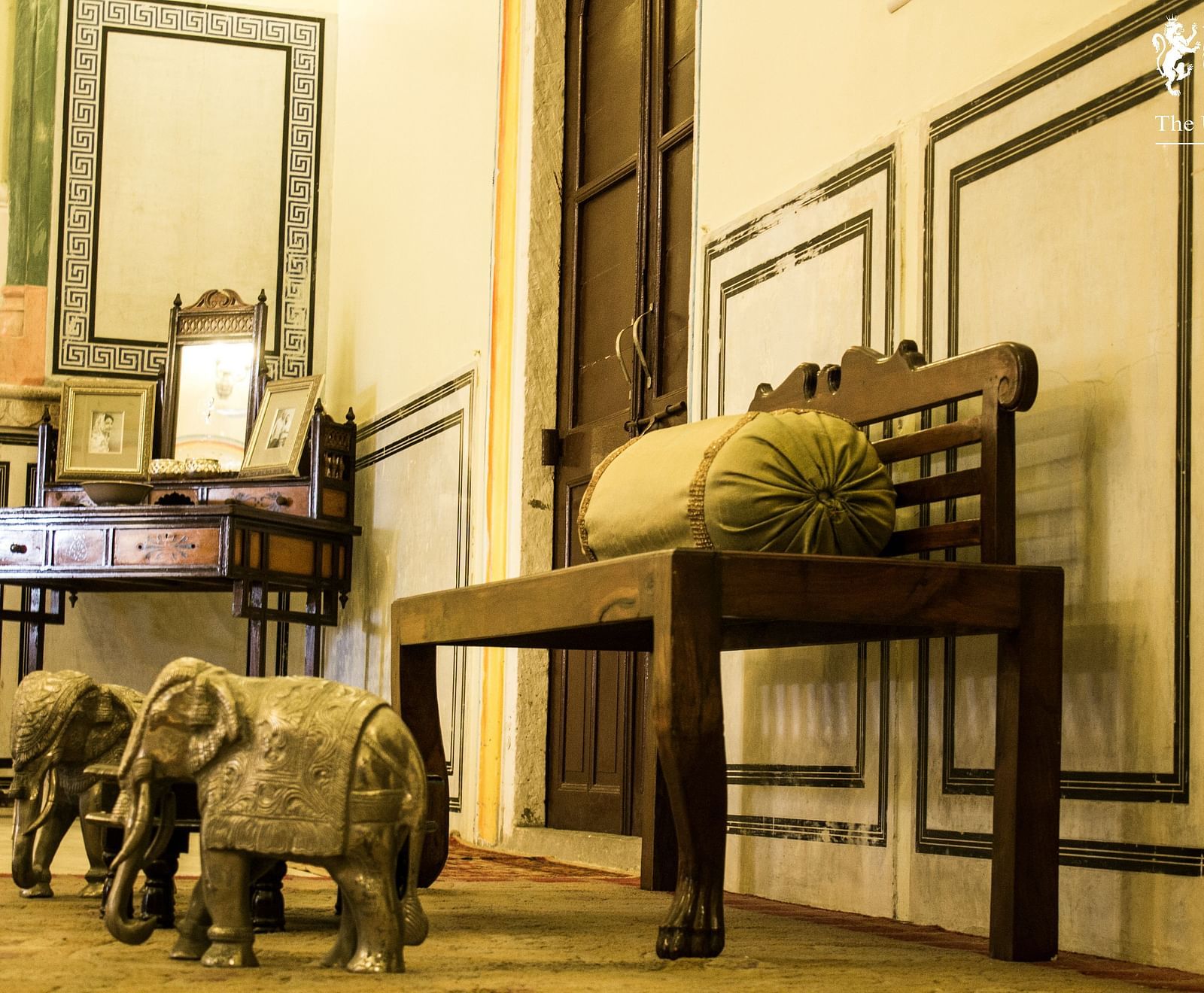 A room at Umaid Vilas Jaipur with a wooden bench, elephant sculptures, and a desk with a mirror.
