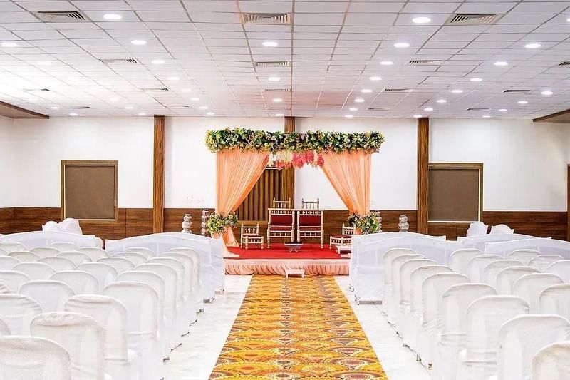 An indoor banquet hall with white chairs arranged for a ceremony at Daksh Resort and Amusement Park.