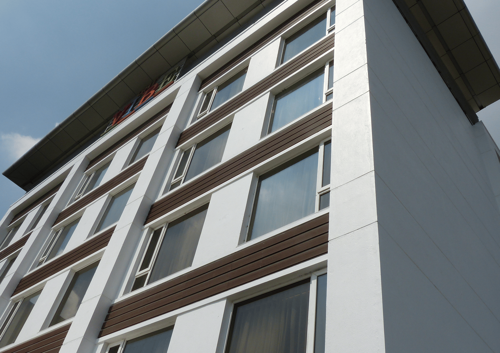 An angular shot of a modern, white, multi-storey building of  Zibe Coimbatore by GRT Hotels with rows of windows and a brown horizontal accent.