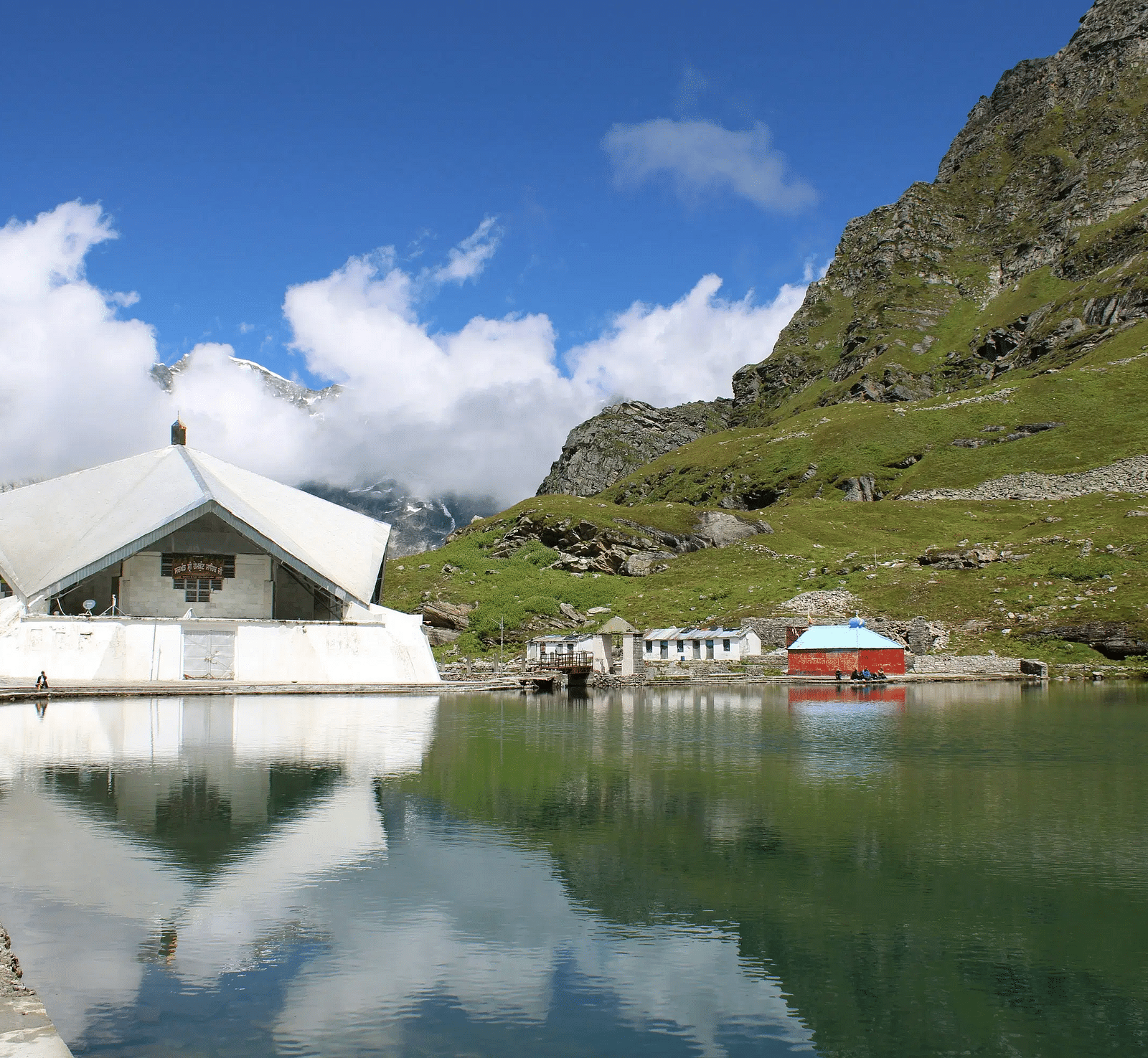 A religious shrine situated on the banks of a lake with a rocky mountain beside it.