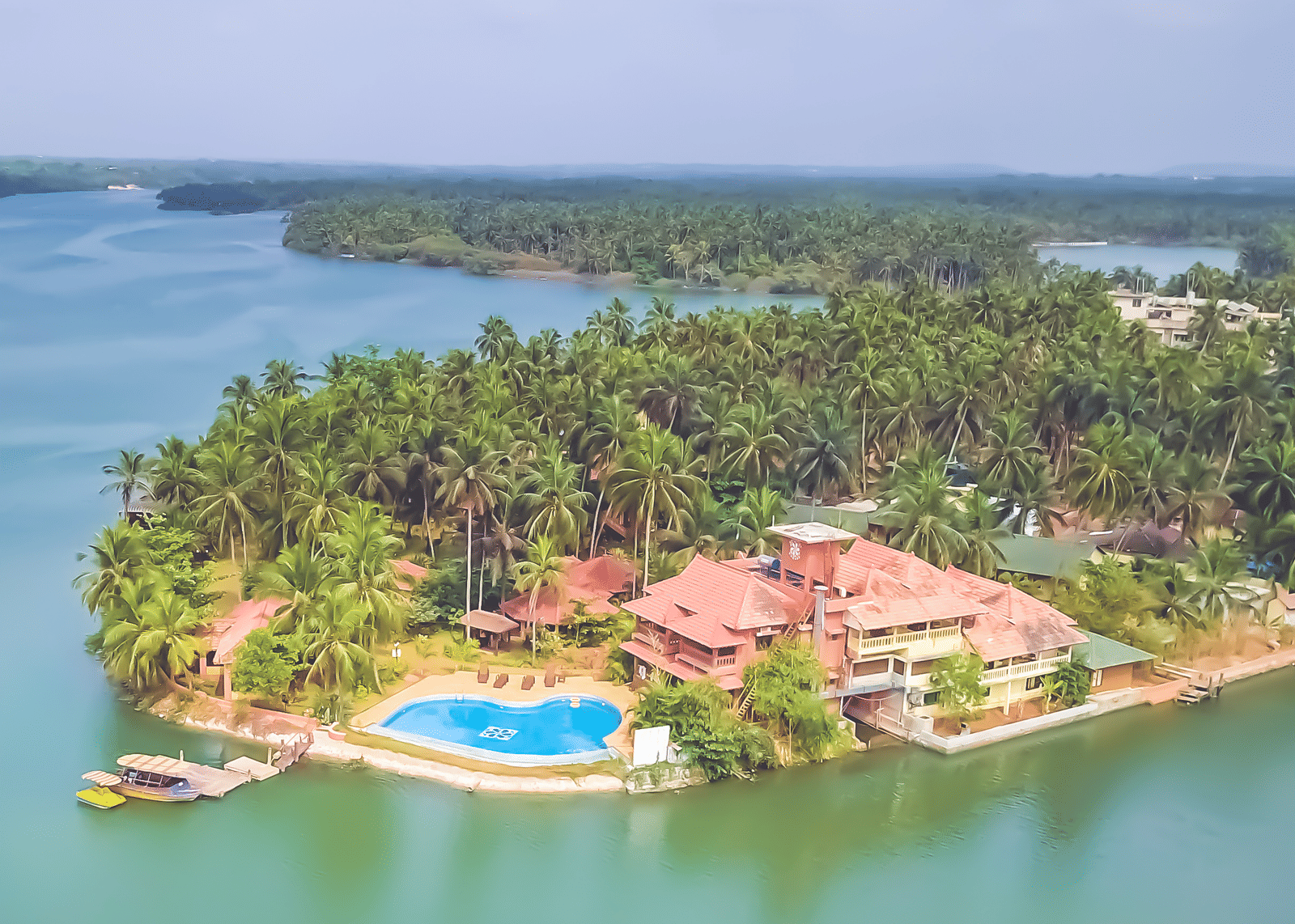 Aerial view of Paradise Lagoon Resort, Udupi, featuring a pool and water all around.