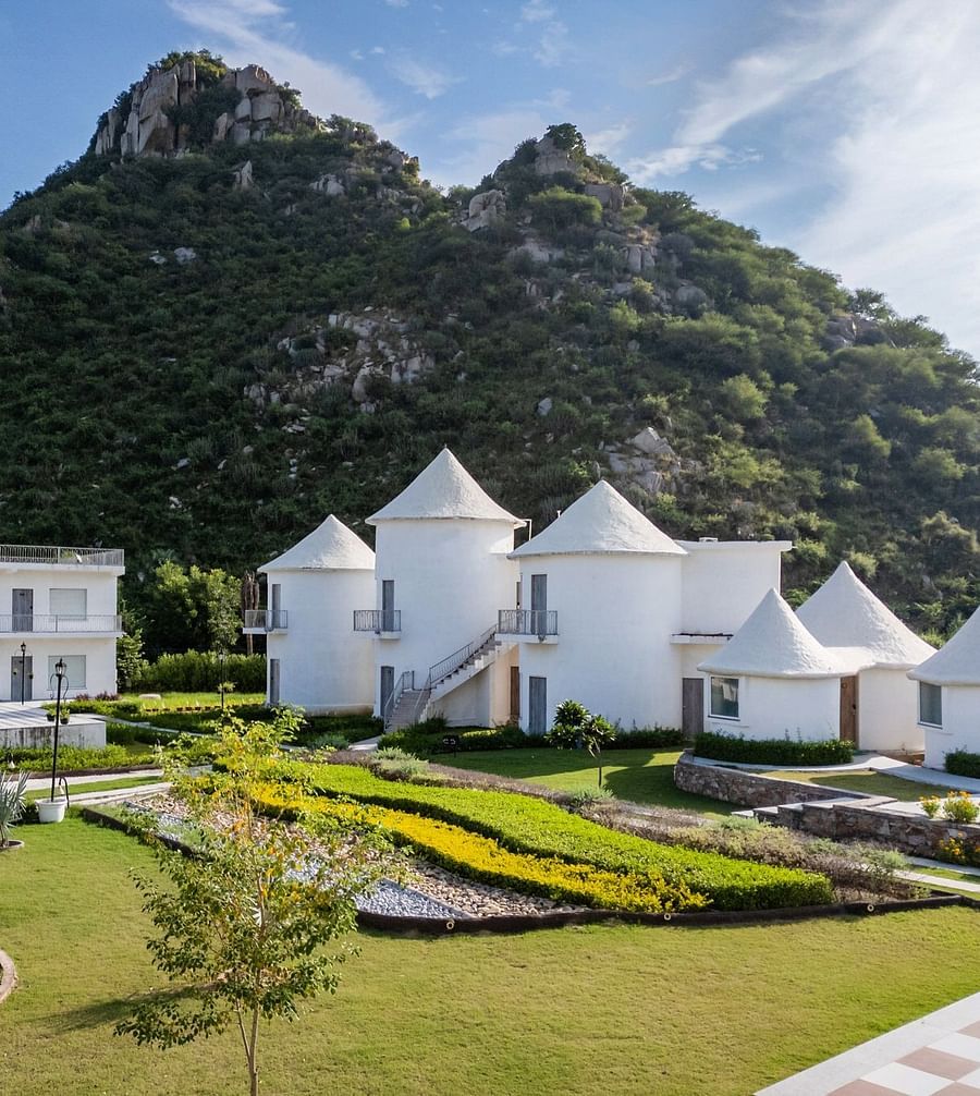 Conical-roof accommodations with an open space in front, set against a scenic mountain backdrop at Valley by Grassfield.