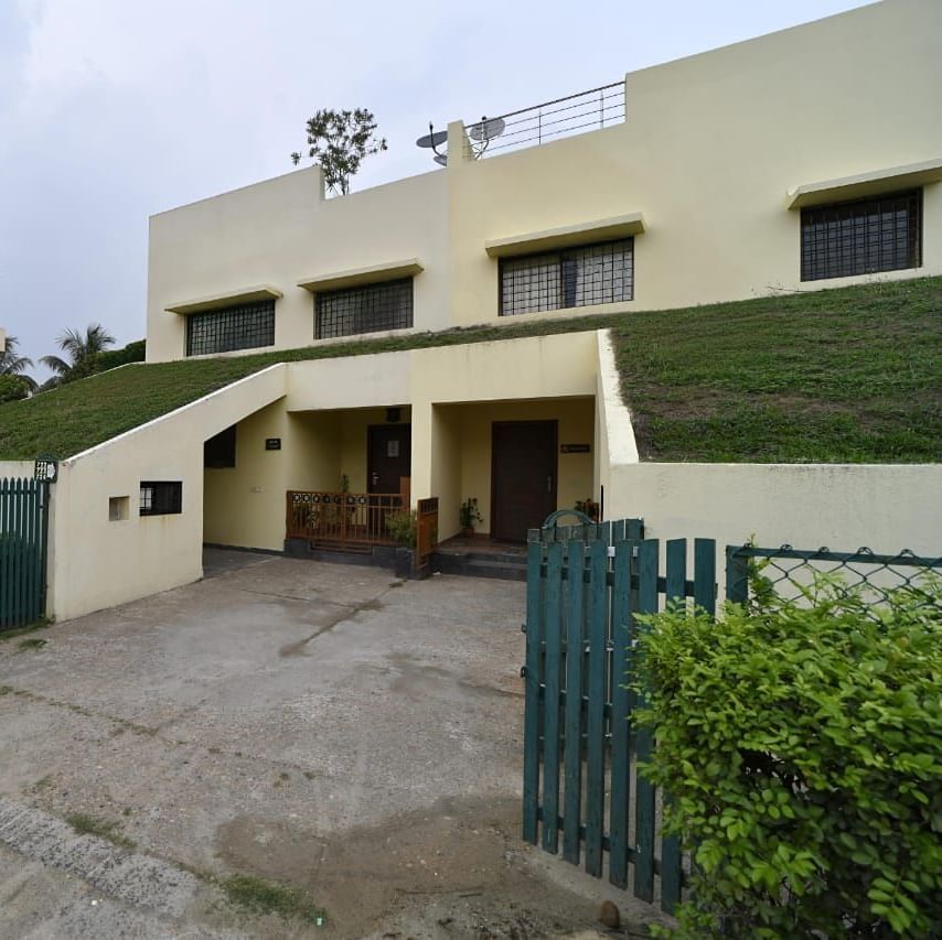 A modern house with a green sloped roof is seen from the outside, featuring a driveway and surrounding greenery | Aqua Bungalow | Vedic Village Spa Resort, Kolkata