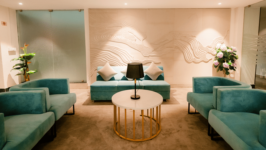 Corner of the business lounge with teal tub chairs, a cushioned sofa, table lamp and frosted glass doors marked The Lounge at Ilara Hotels & Spa, Tada.