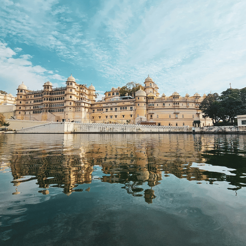 City Palace building reflected in the still waters of Lake Pichola under a bright blue sky
