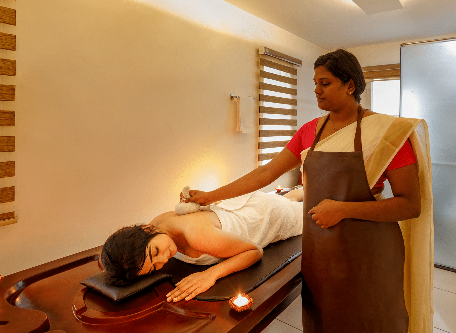 A person receiving a massage treatment on a wooden table in a softly lit room with brick accents.