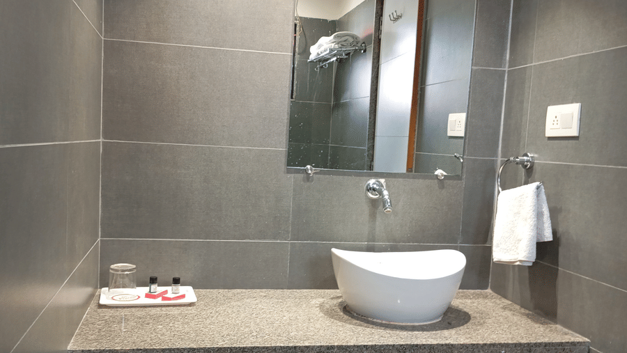 A bathroom vanity area at Hotel Ashray Inn Express showcasing a countertop wash basin, mirror, towel rail, and sleek finishes.
